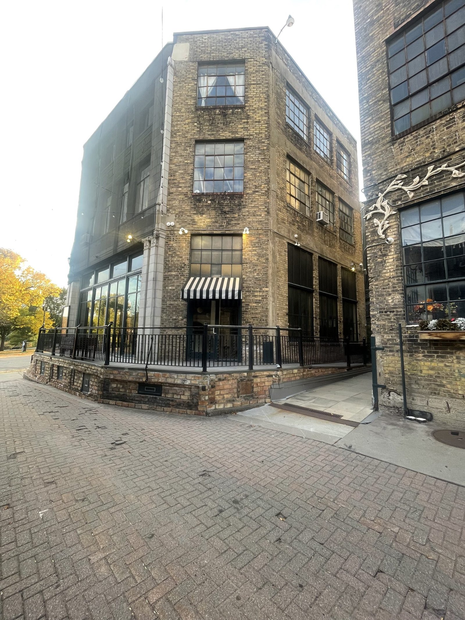 Three-story yellow brick building with large steel-frame windows and a striped awning at Loring Corners