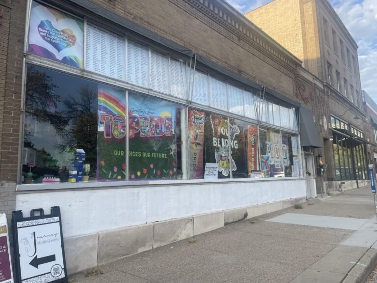 Storefront window covered with Twin Cities Pride posters and a list of supporters’ names